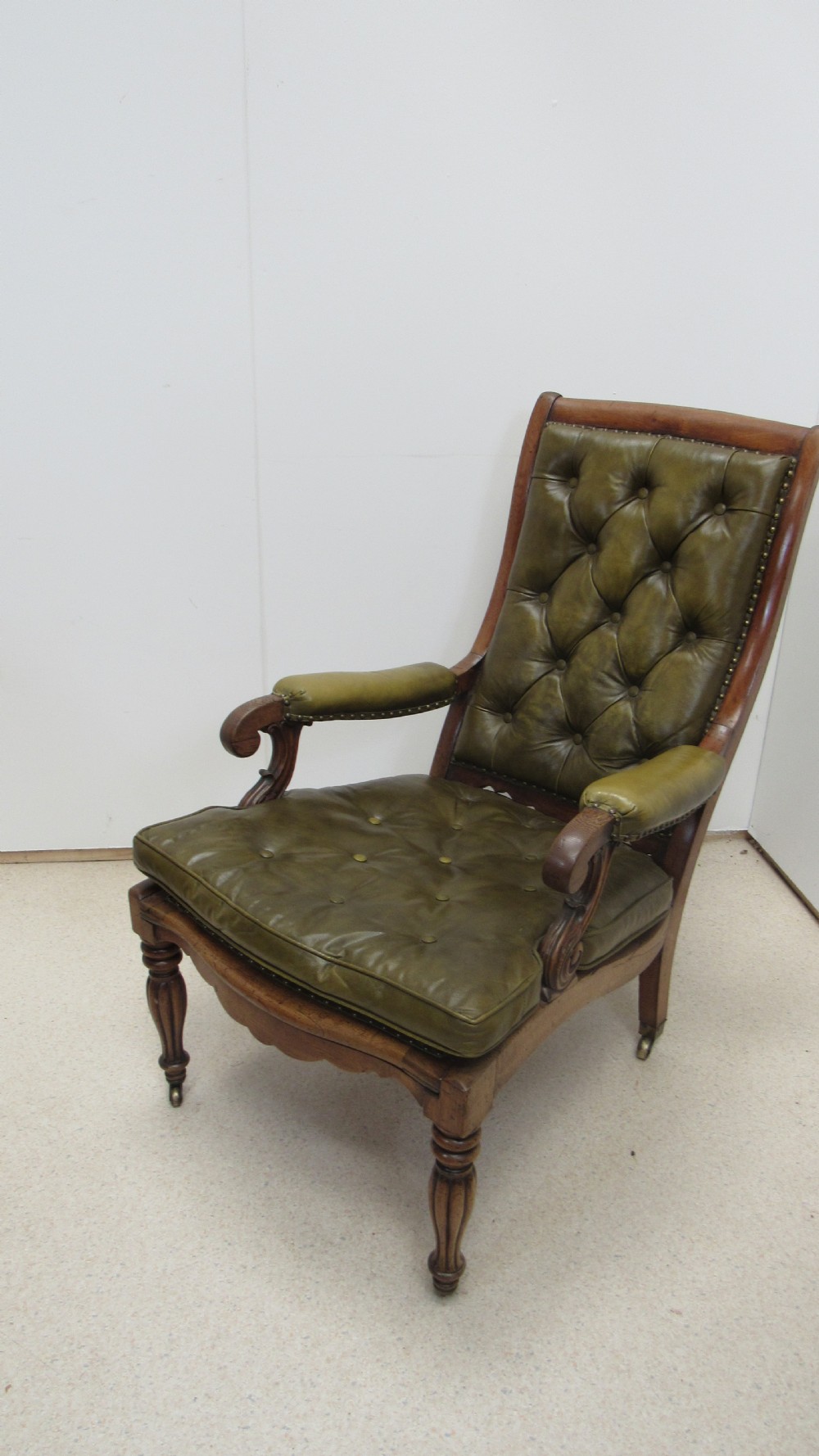 A William IV mahogany library chair upholstered in deep-buttoned olive green leather with padded scroll arms and turned front legs on brass castors.