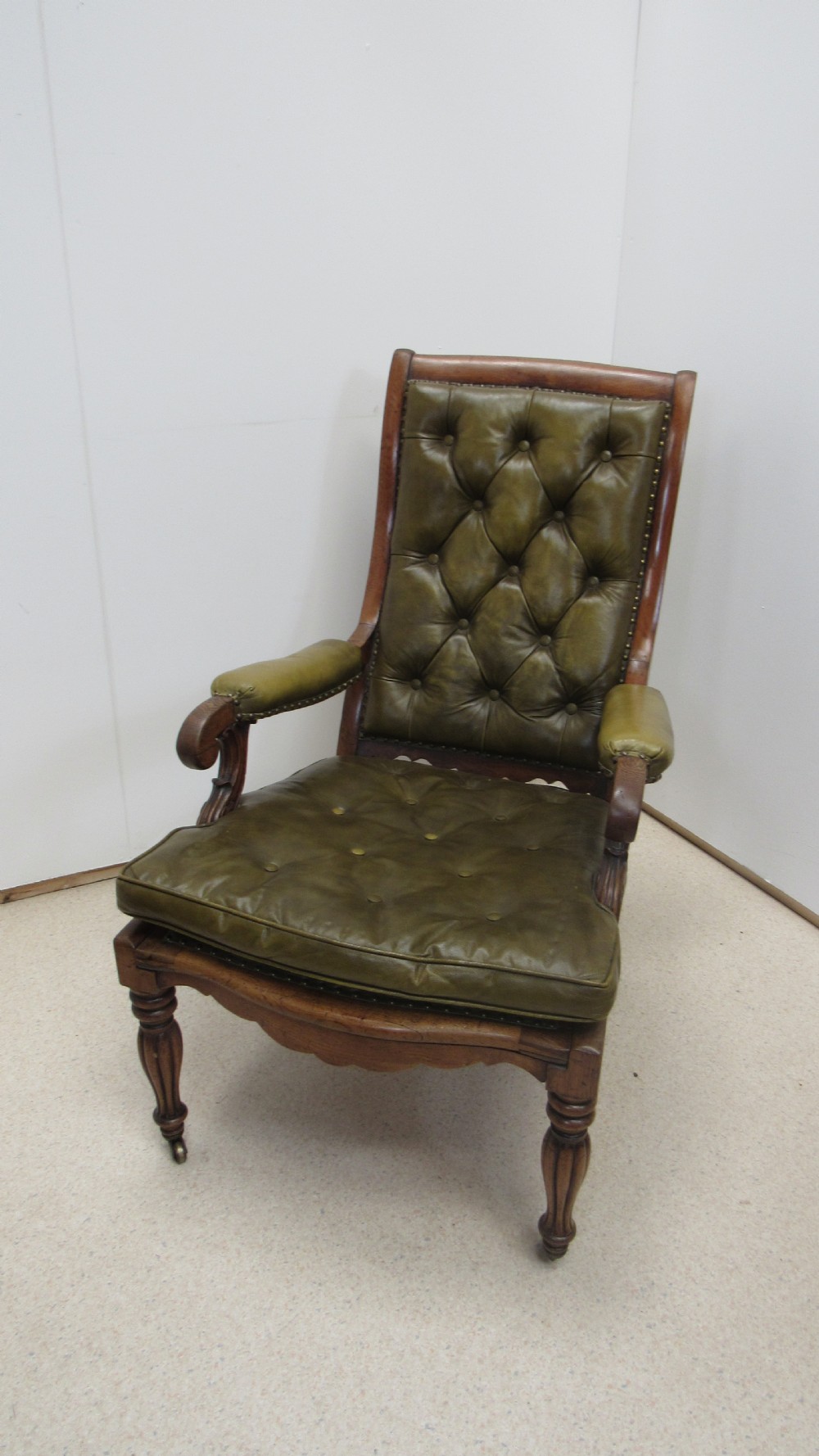 A William IV mahogany library chair upholstered in deep-buttoned olive green leather with padded scroll arms and turned front legs on brass castors. View II