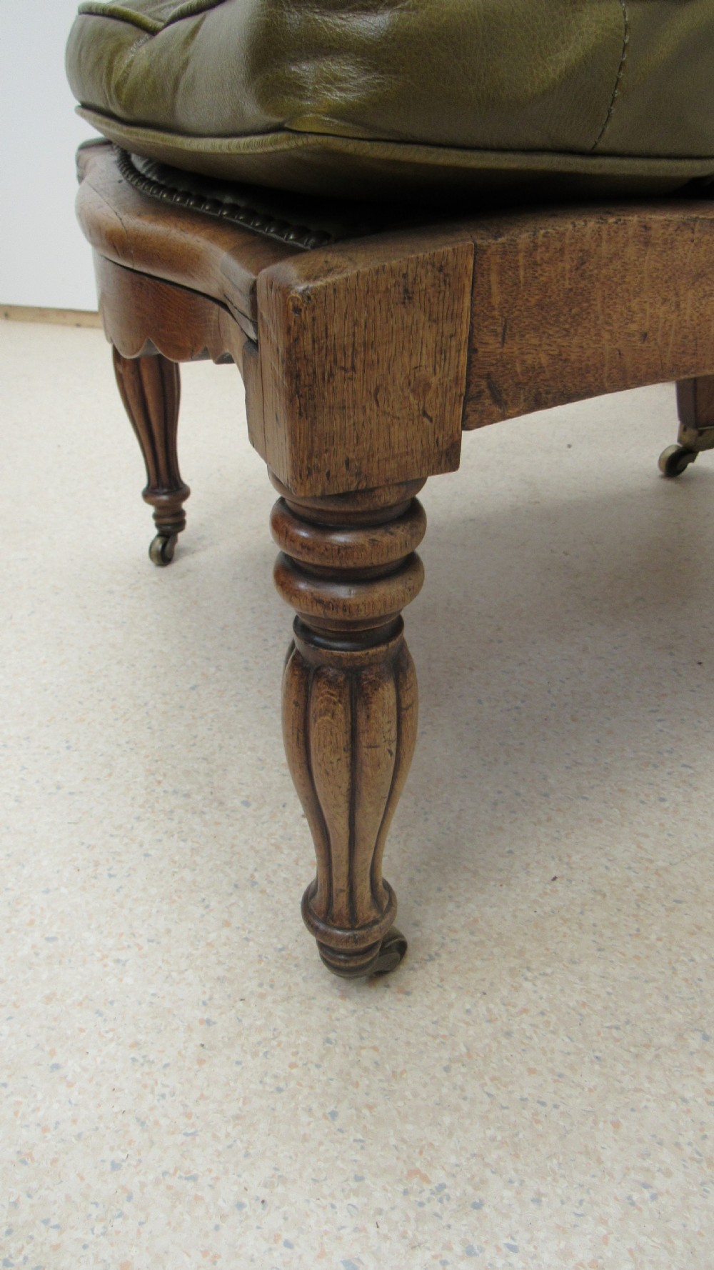 A William IV mahogany library chair upholstered in deep-buttoned olive green leather with padded scroll arms and turned front legs on brass castors. View V