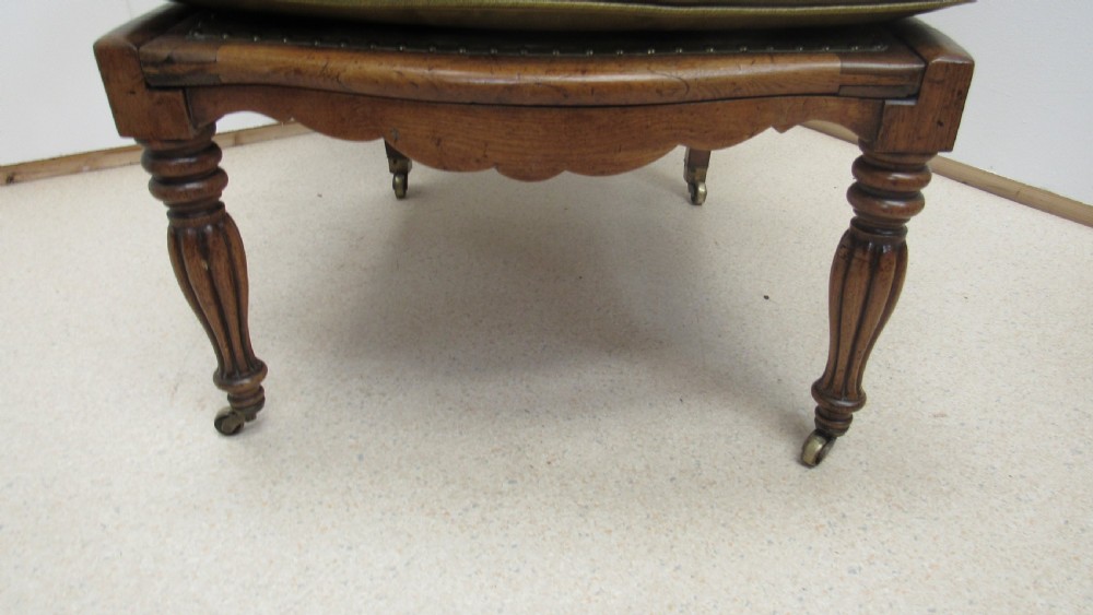 A William IV mahogany library chair upholstered in deep-buttoned olive green leather with padded scroll arms and turned front legs on brass castors. View VI