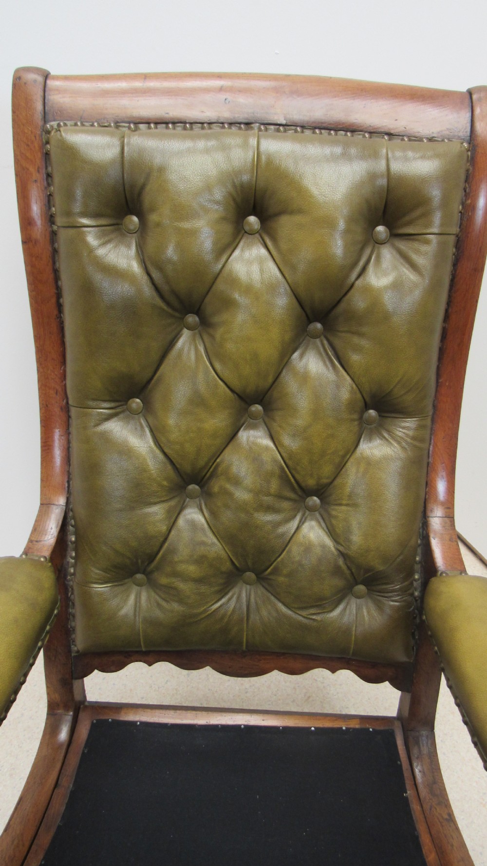 A William IV mahogany library chair upholstered in deep-buttoned olive green leather with padded scroll arms and turned front legs on brass castors. View IX
