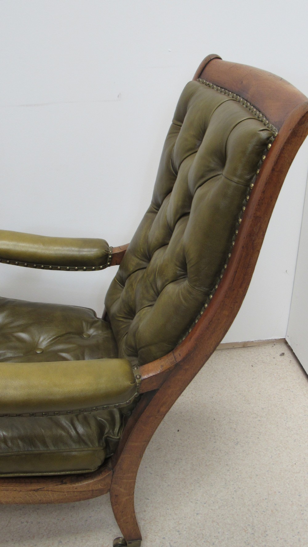 A William IV mahogany library chair upholstered in deep-buttoned olive green leather with padded scroll arms and turned front legs on brass castors. View XII