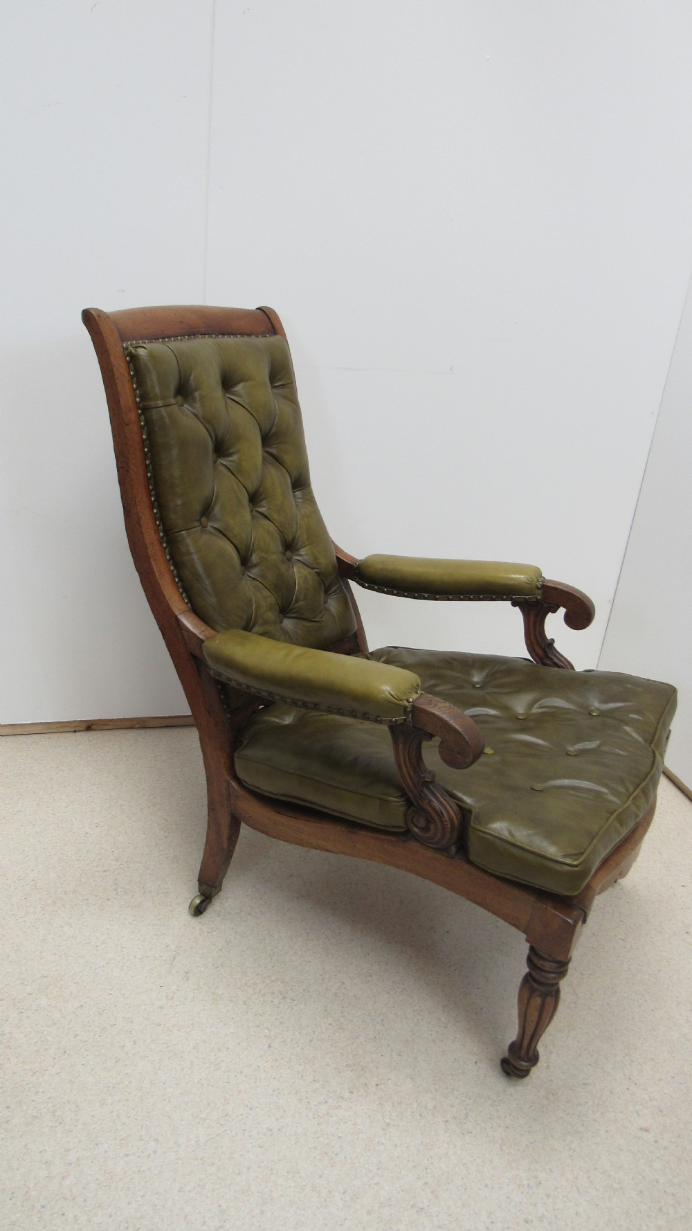 A William IV mahogany library chair upholstered in deep-buttoned olive green leather with padded scroll arms and turned front legs on brass castors. View XIII