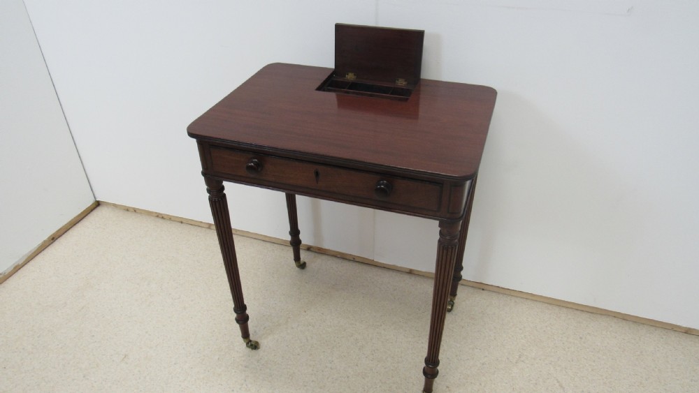 A Regency mahogany chamber table featuring reeded tapered legs on brass castors, a central drawer with wooden knobs, and a hinged lid top. View III