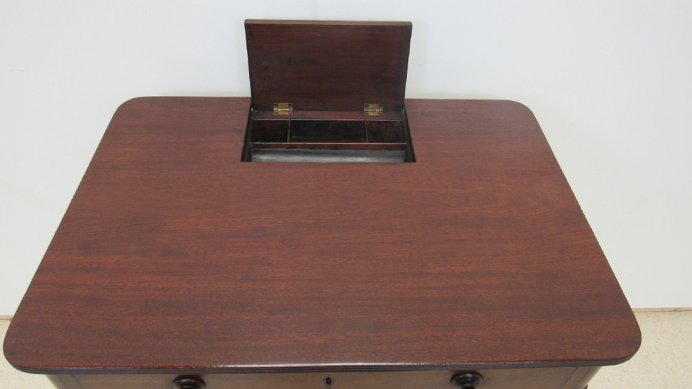 A Regency mahogany chamber table featuring reeded tapered legs on brass castors, a central drawer with wooden knobs, and a hinged lid top. View V