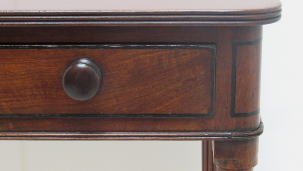 A Regency mahogany chamber table featuring reeded tapered legs on brass castors, a central drawer with wooden knobs, and a hinged lid top. View VII
