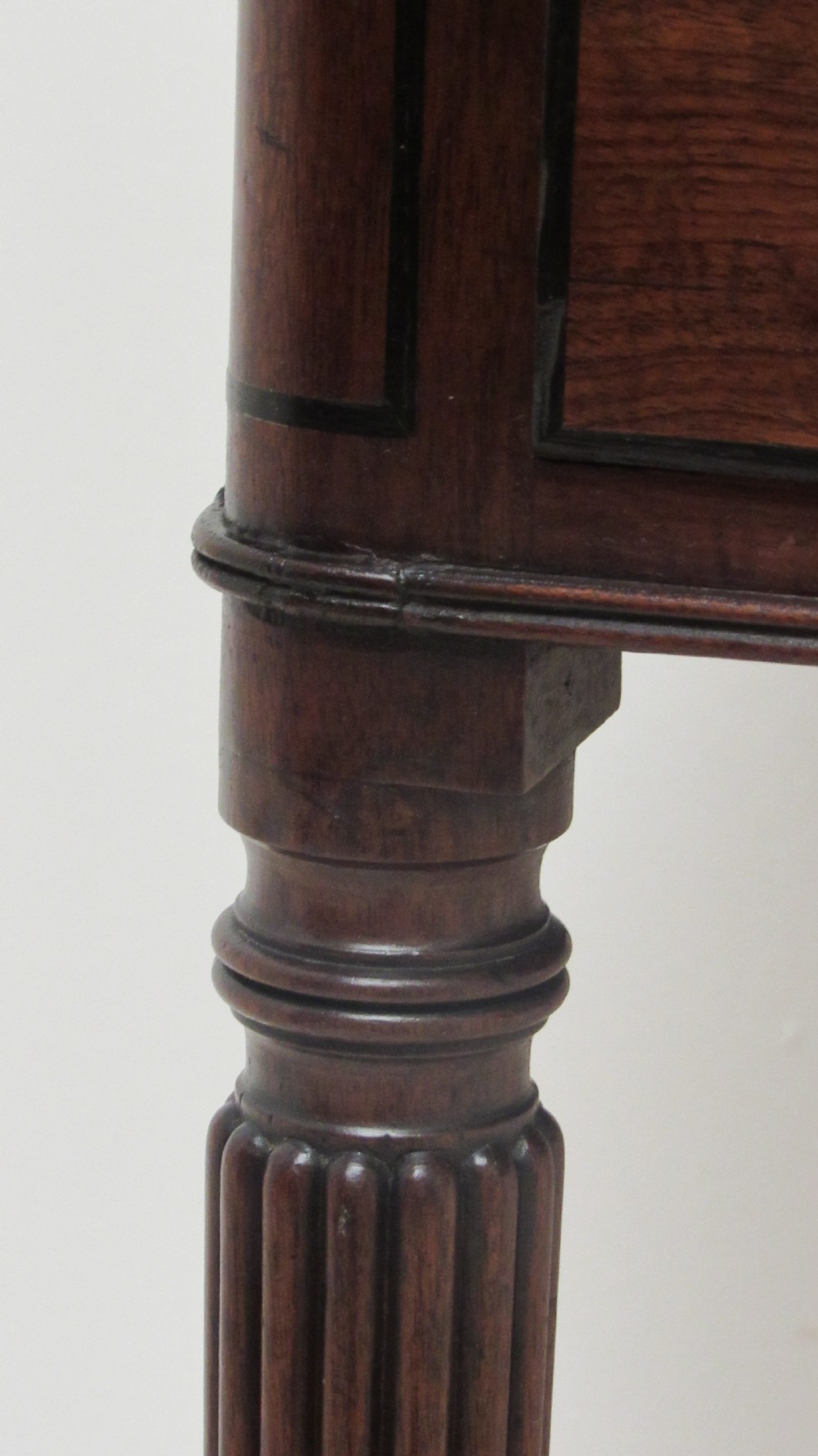 A Regency mahogany chamber table featuring reeded tapered legs on brass castors, a central drawer with wooden knobs, and a hinged lid top. View XI