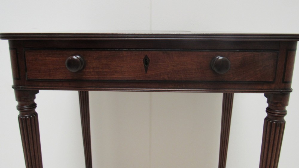 A Regency mahogany chamber table featuring reeded tapered legs on brass castors, a central drawer with wooden knobs, and a hinged lid top. View XII