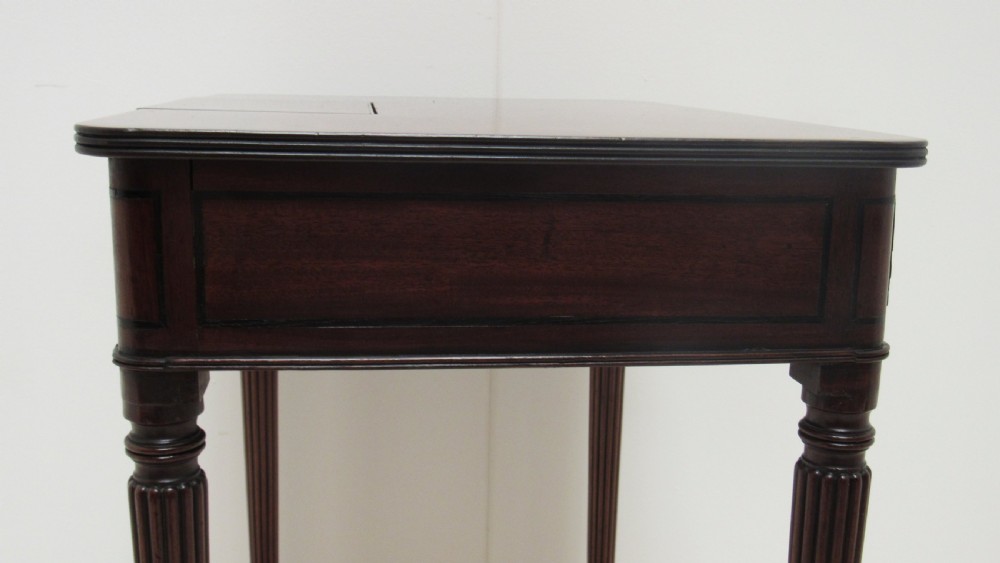 A Regency mahogany chamber table featuring reeded tapered legs on brass castors, a central drawer with wooden knobs, and a hinged lid top. View XV