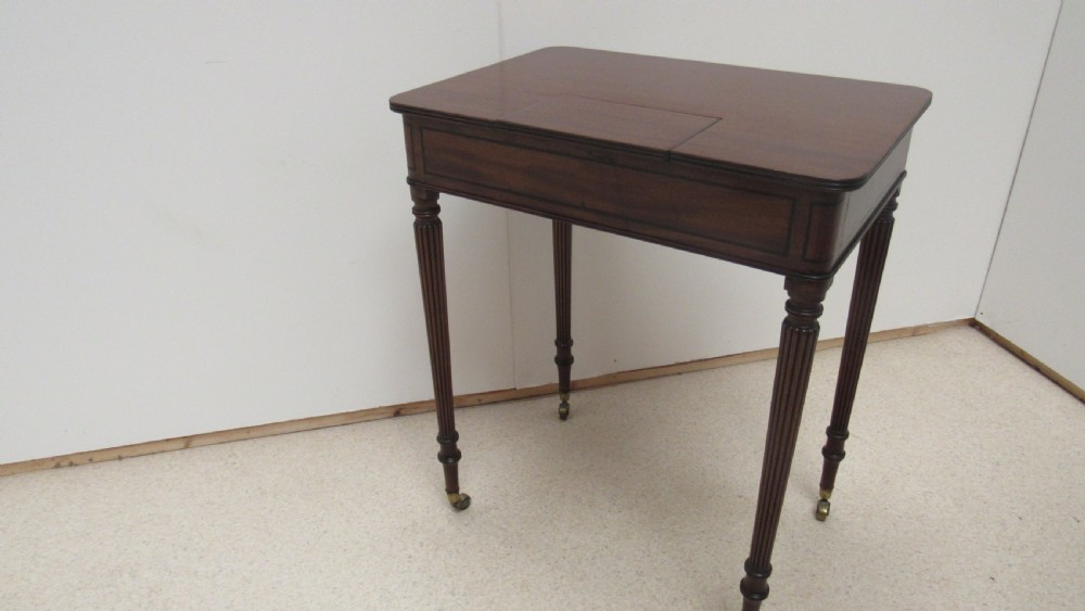 A Regency mahogany chamber table featuring reeded tapered legs on brass castors, a central drawer with wooden knobs, and a hinged lid top. View XVII