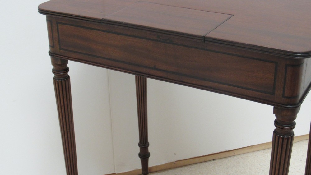 A Regency mahogany chamber table featuring reeded tapered legs on brass castors, a central drawer with wooden knobs, and a hinged lid top. View XVIII