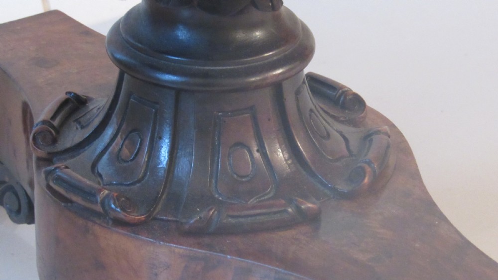 An antique Victorian walnut writing centre table featuring a figured top, deeply carved foliate apron, and carved turned end supports on a trestle base. View VIII