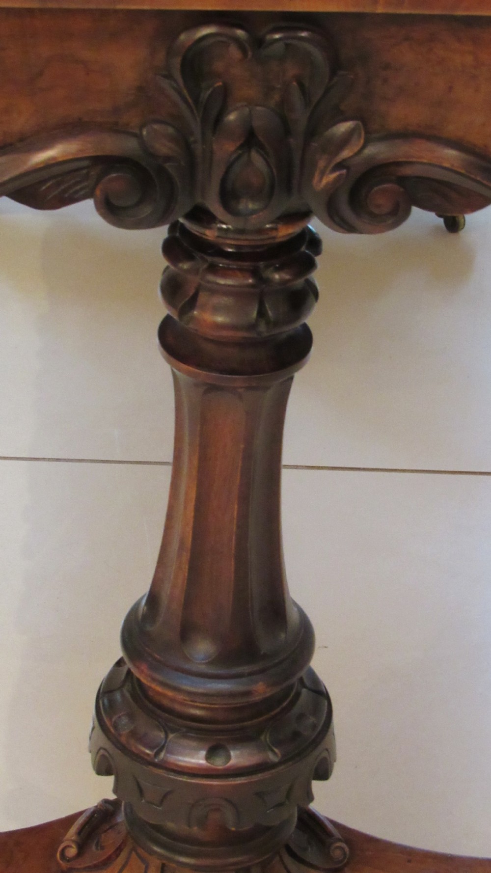 An antique Victorian walnut writing centre table featuring a figured top, deeply carved foliate apron, and carved turned end supports on a trestle base. View XVII