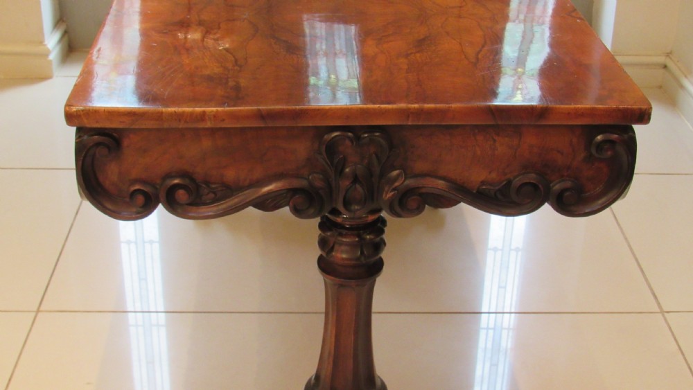 An antique Victorian walnut writing centre table featuring a figured top, deeply carved foliate apron, and carved turned end supports on a trestle base. View XVIII
