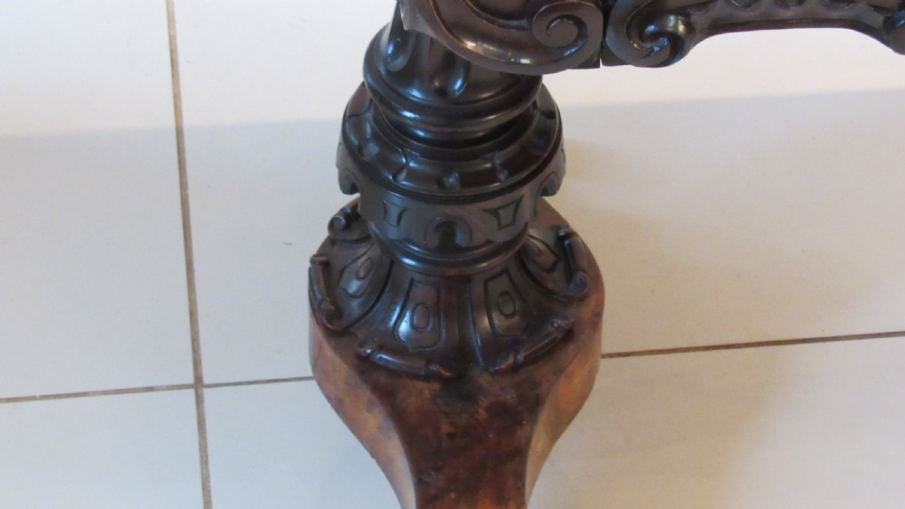 An antique Victorian walnut writing centre table featuring a figured top, deeply carved foliate apron, and carved turned end supports on a trestle base. View XXIII