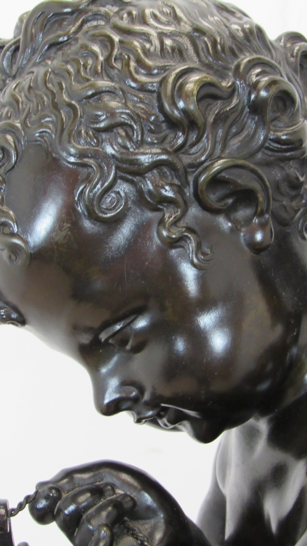 A dark patinated bronze figure of a winged cherub seated on a rock while holding a bow, set upon a rectangular reddish marble plinth. View II