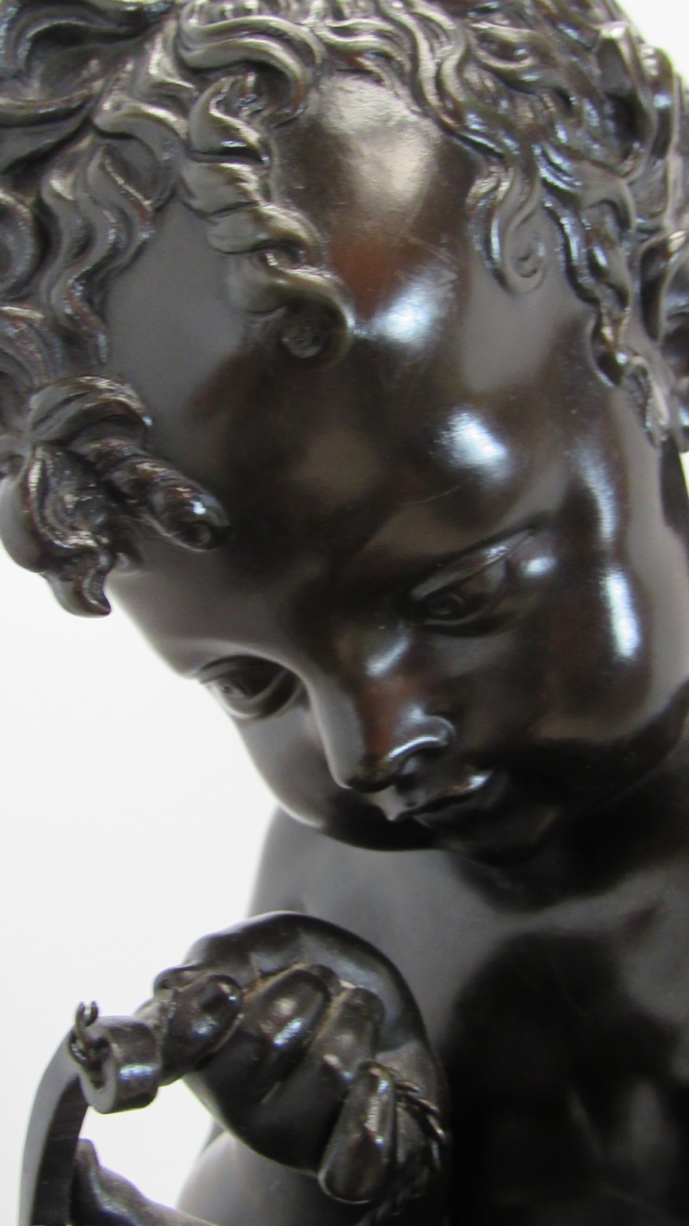 A dark patinated bronze figure of a winged cherub seated on a rock while holding a bow, set upon a rectangular reddish marble plinth. View IV