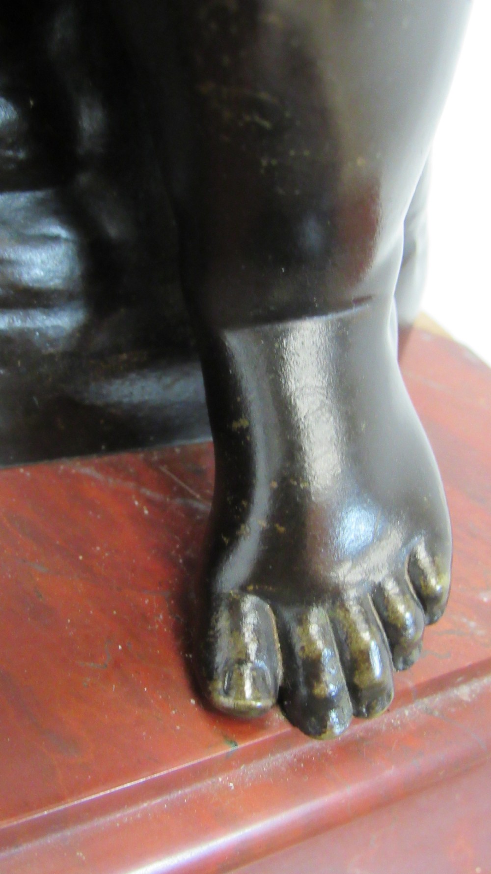 A dark patinated bronze figure of a winged cherub seated on a rock while holding a bow, set upon a rectangular reddish marble plinth. View VI