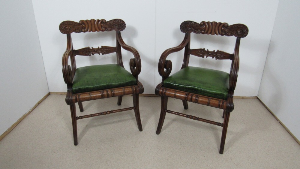 A pair of carved mahogany armchairs featuring scroll-carved top rails, curved armrests, reeded front rails, and green leather upholstered seats.