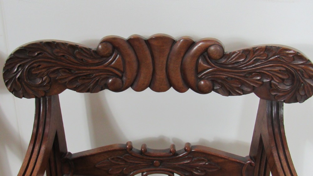A pair of carved mahogany armchairs featuring scroll-carved top rails, curved armrests, reeded front rails, and green leather upholstered seats. View X