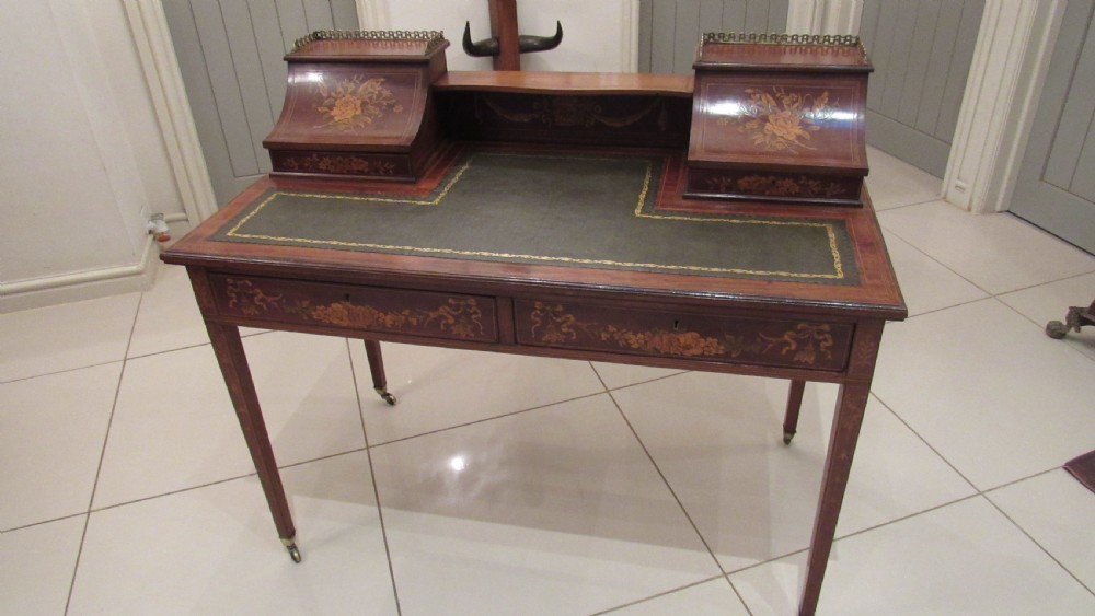 An Edwardian mahogany writing desk featuring detailed floral marquetry inlays, a green leather top, and raised stationery boxes with brass galleries.