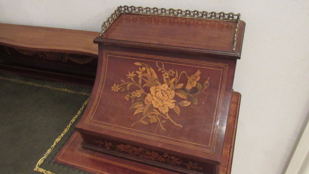An Edwardian mahogany writing desk featuring detailed floral marquetry inlays, a green leather top, and raised stationery boxes with brass galleries. View V