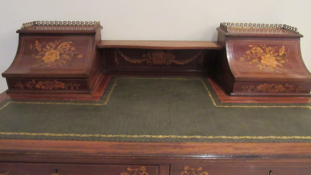 An Edwardian mahogany writing desk featuring detailed floral marquetry inlays, a green leather top, and raised stationery boxes with brass galleries. View VI