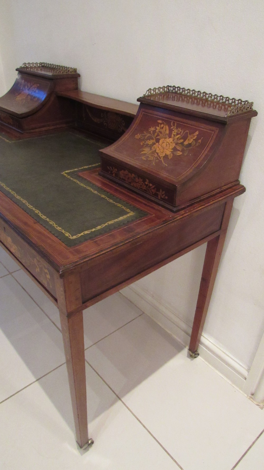 An Edwardian mahogany writing desk featuring detailed floral marquetry inlays, a green leather top, and raised stationery boxes with brass galleries. View XVI