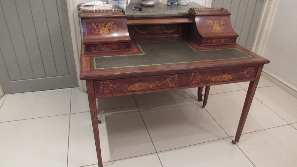 An Edwardian mahogany writing desk featuring detailed floral marquetry inlays, a green leather top, and raised stationery boxes with brass galleries. View XIX