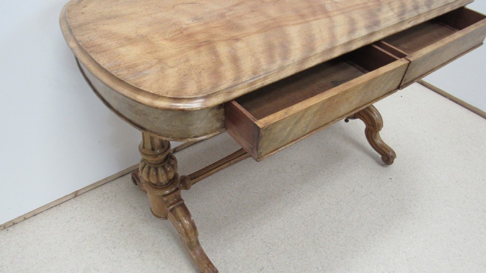 A Victorian satin walnut library table featuring a rectangular top with rounded corners, a pulled-out frieze drawer, turned pedestal legs, and a low central stretcher base. View VI