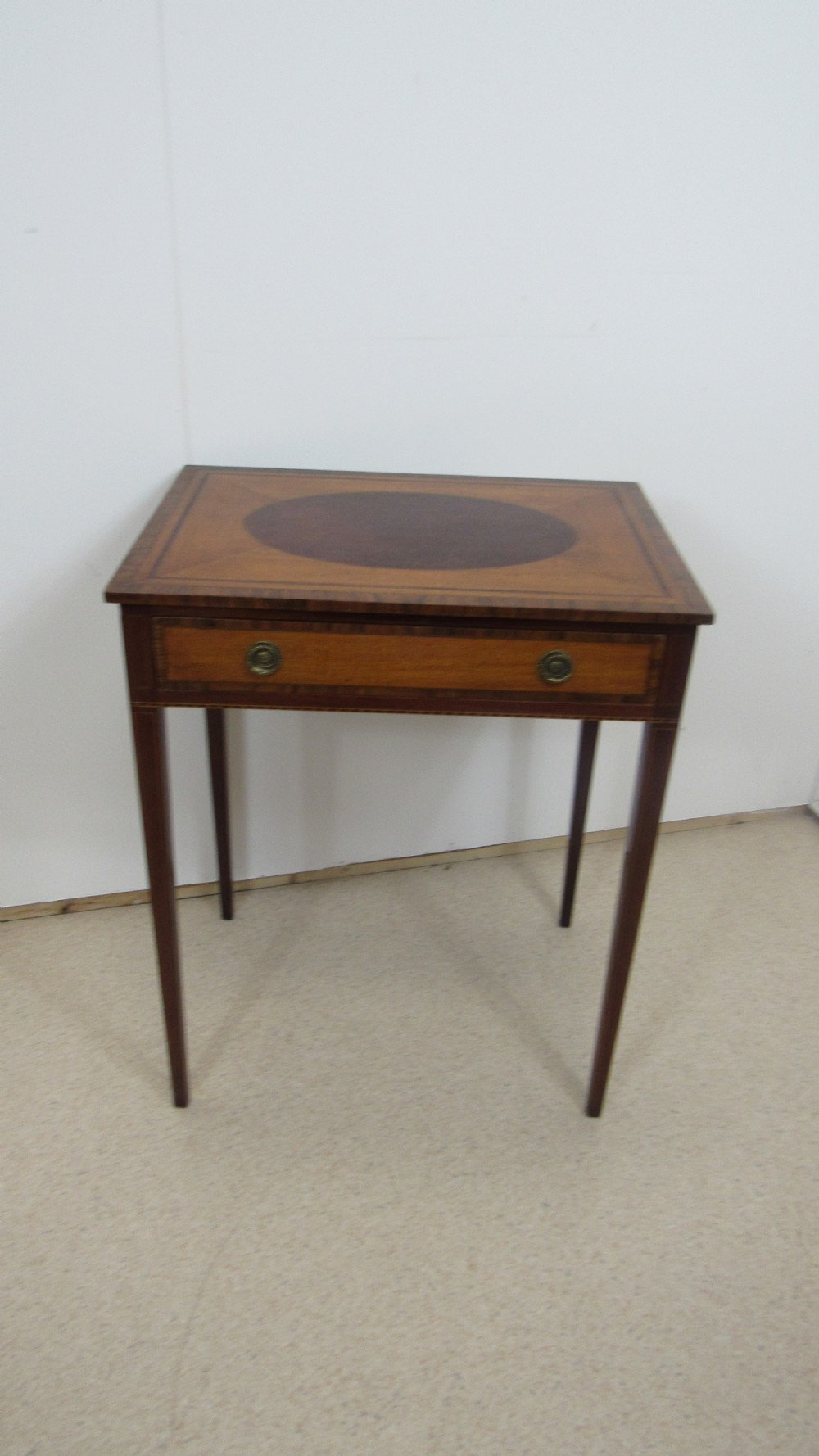 A 19th-century wooden side table featuring square tapered legs, a single drawer with brass handles, and a decorative oval inlaid top surface.
