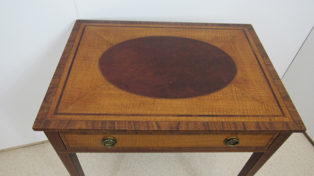 A 19th-century wooden side table featuring square tapered legs, a single drawer with brass handles, and a decorative oval inlaid top surface. View II