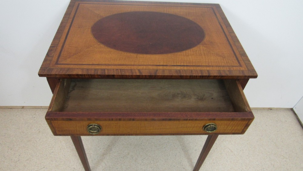 A 19th-century wooden side table featuring square tapered legs, a single drawer with brass handles, and a decorative oval inlaid top surface. View XI