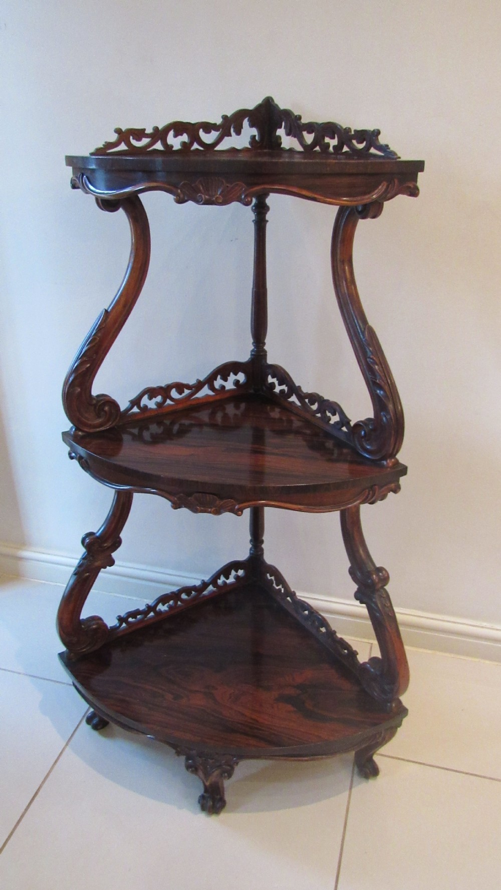 A three-tiered Victorian rosewood corner whatnot featuring intricate carved fretwork galleries, serpentine supports, and small carved feet. View II