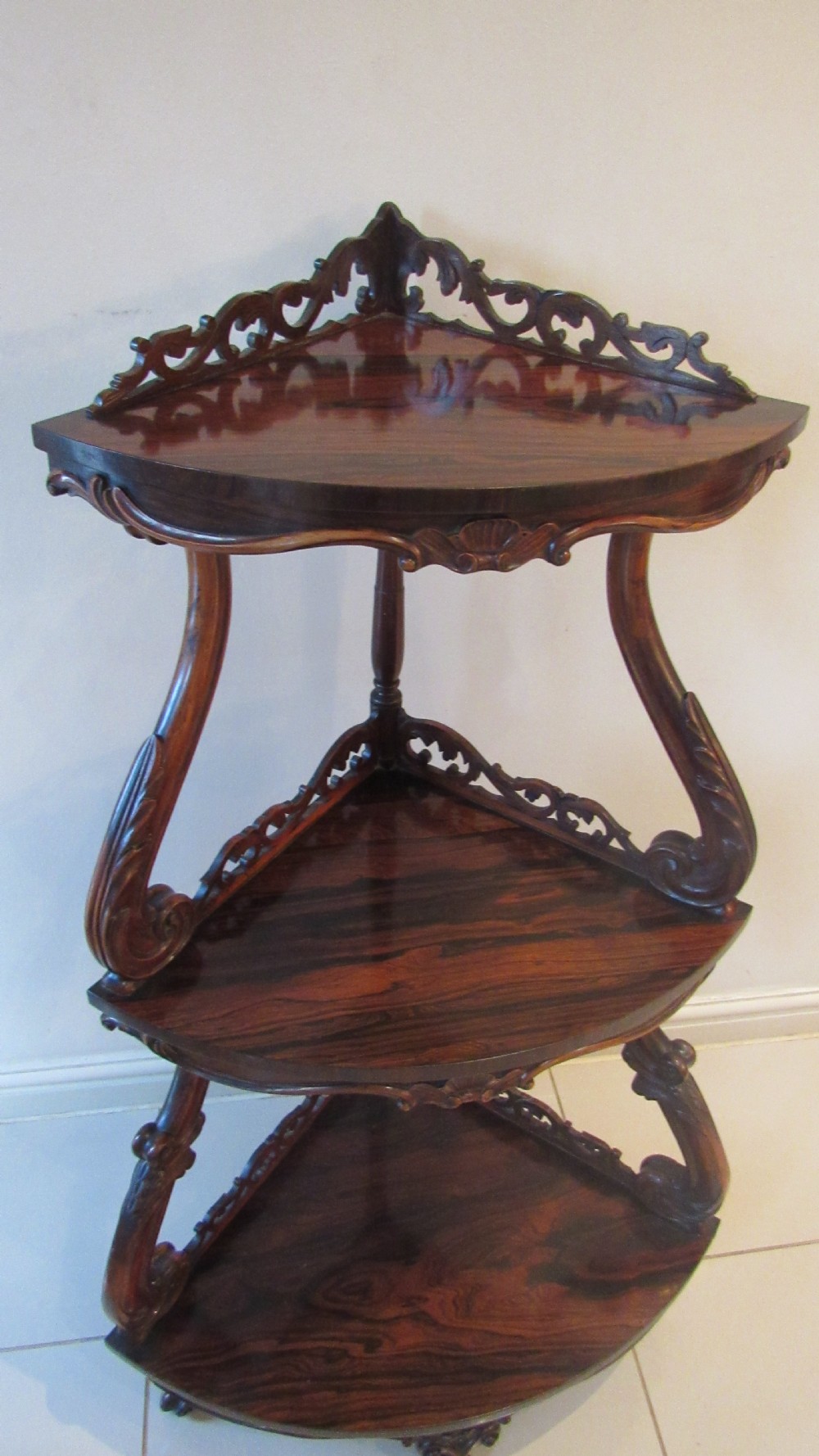A three-tiered Victorian rosewood corner whatnot featuring intricate carved fretwork galleries, serpentine supports, and small carved feet. View XIV
