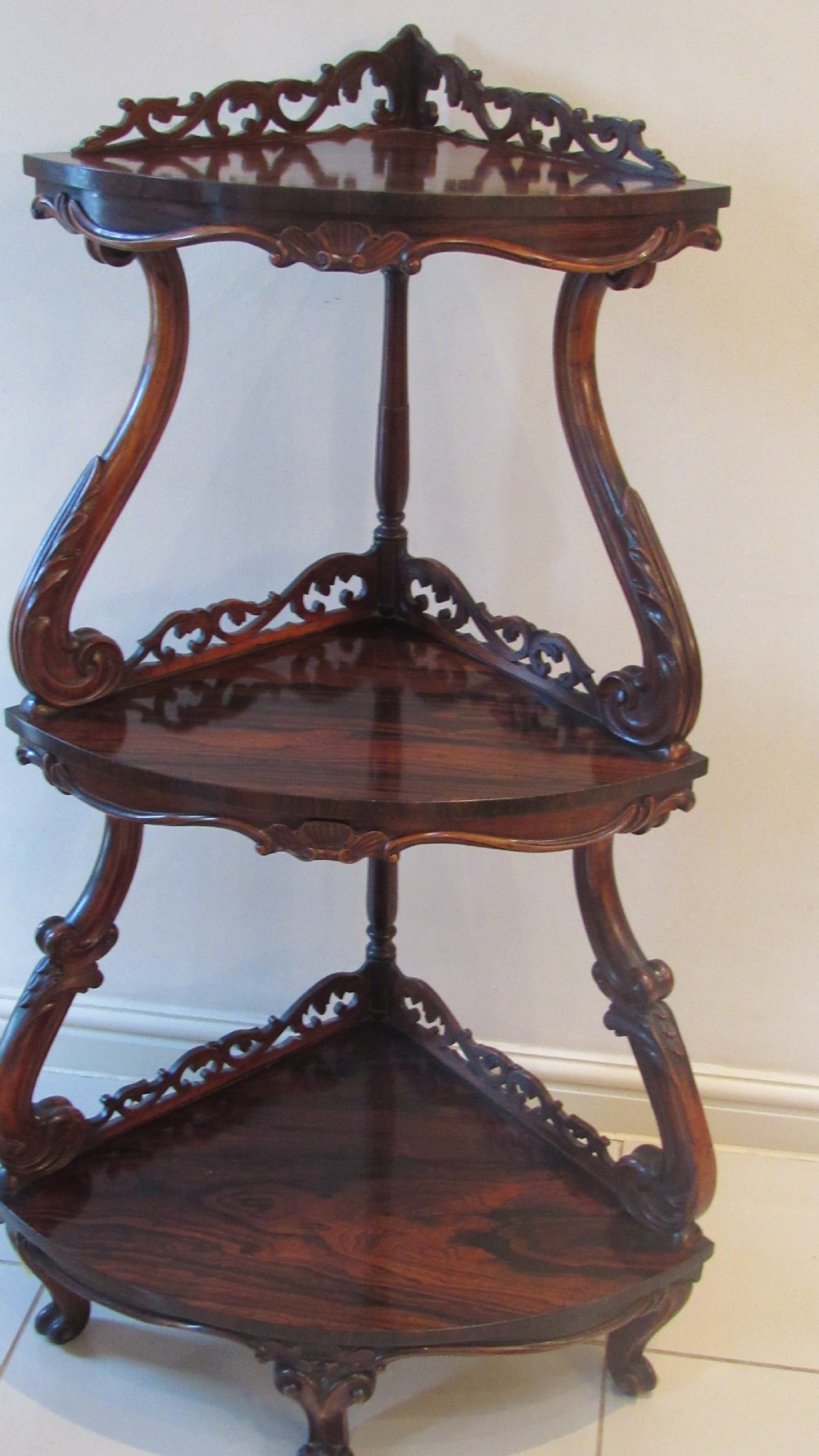A three-tiered Victorian rosewood corner whatnot featuring intricate carved fretwork galleries, serpentine supports, and small carved feet. View XVIII
