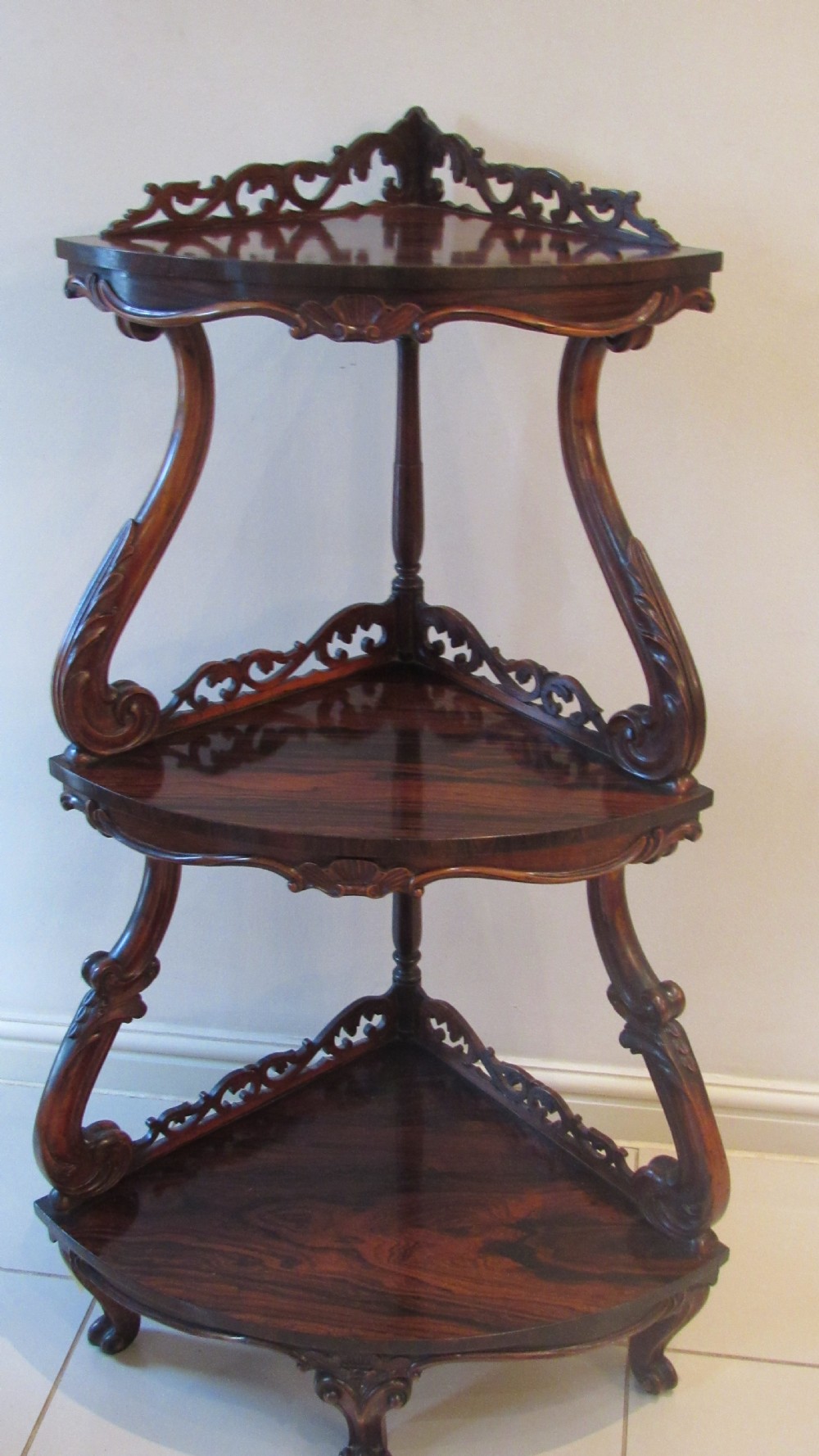 A three-tiered Victorian rosewood corner whatnot featuring intricate carved fretwork galleries, serpentine supports, and small carved feet. View XIX