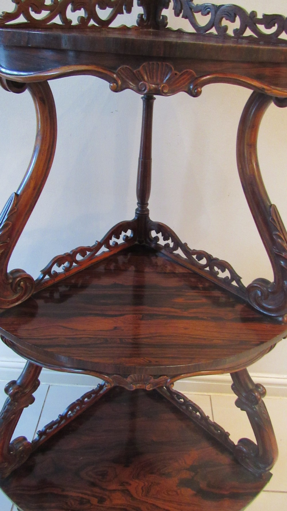 A three-tiered Victorian rosewood corner whatnot featuring intricate carved fretwork galleries, serpentine supports, and small carved feet. View XX