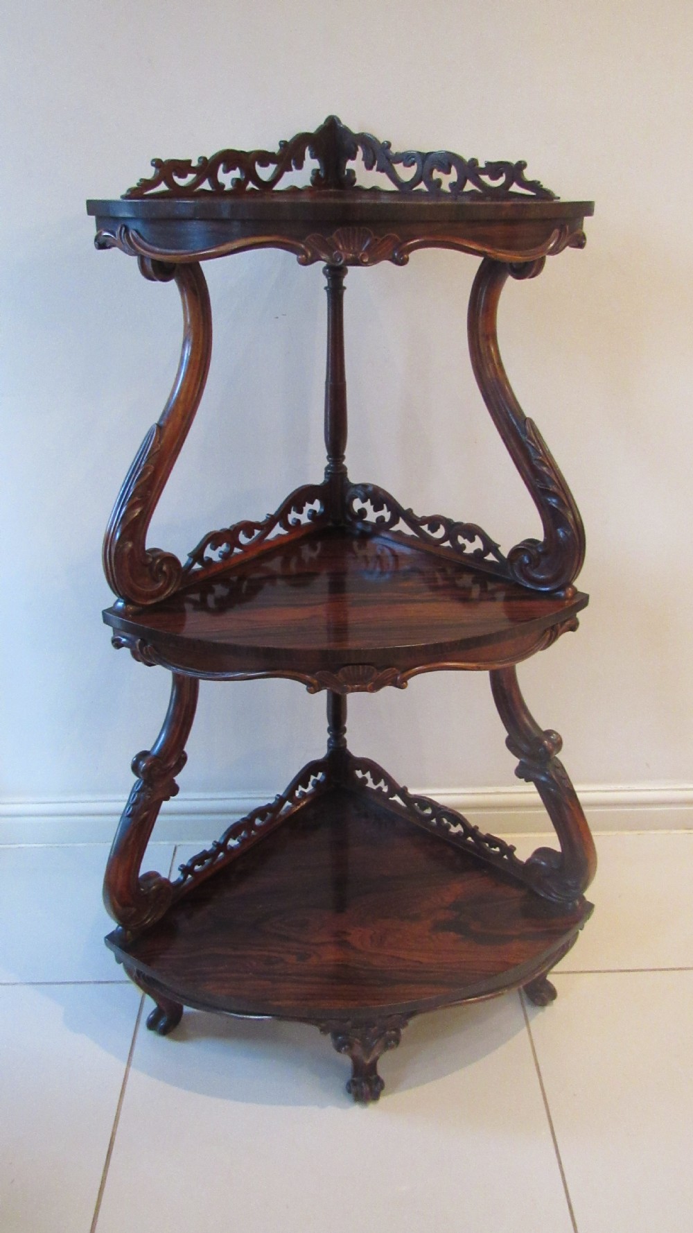 A three-tiered Victorian rosewood corner whatnot featuring intricate carved fretwork galleries, serpentine supports, and small carved feet. View XXI