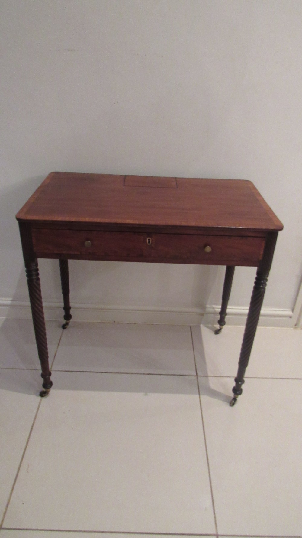 A Georgian mahogany chamber table featuring a rectangular top with a central flap, a single frieze drawer with brass hardware, and spiral turned legs on brass castors. View II