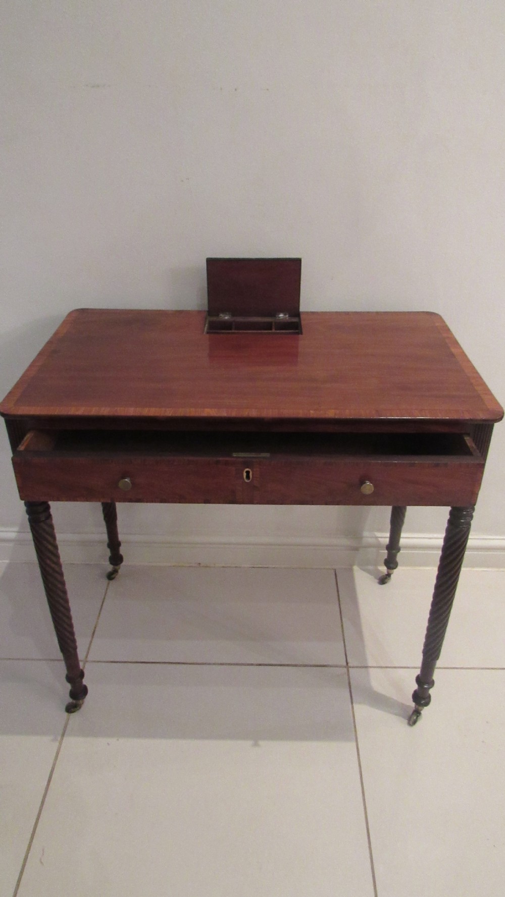 A Georgian mahogany chamber table featuring a rectangular top with a central flap, a single frieze drawer with brass hardware, and spiral turned legs on brass castors. View III
