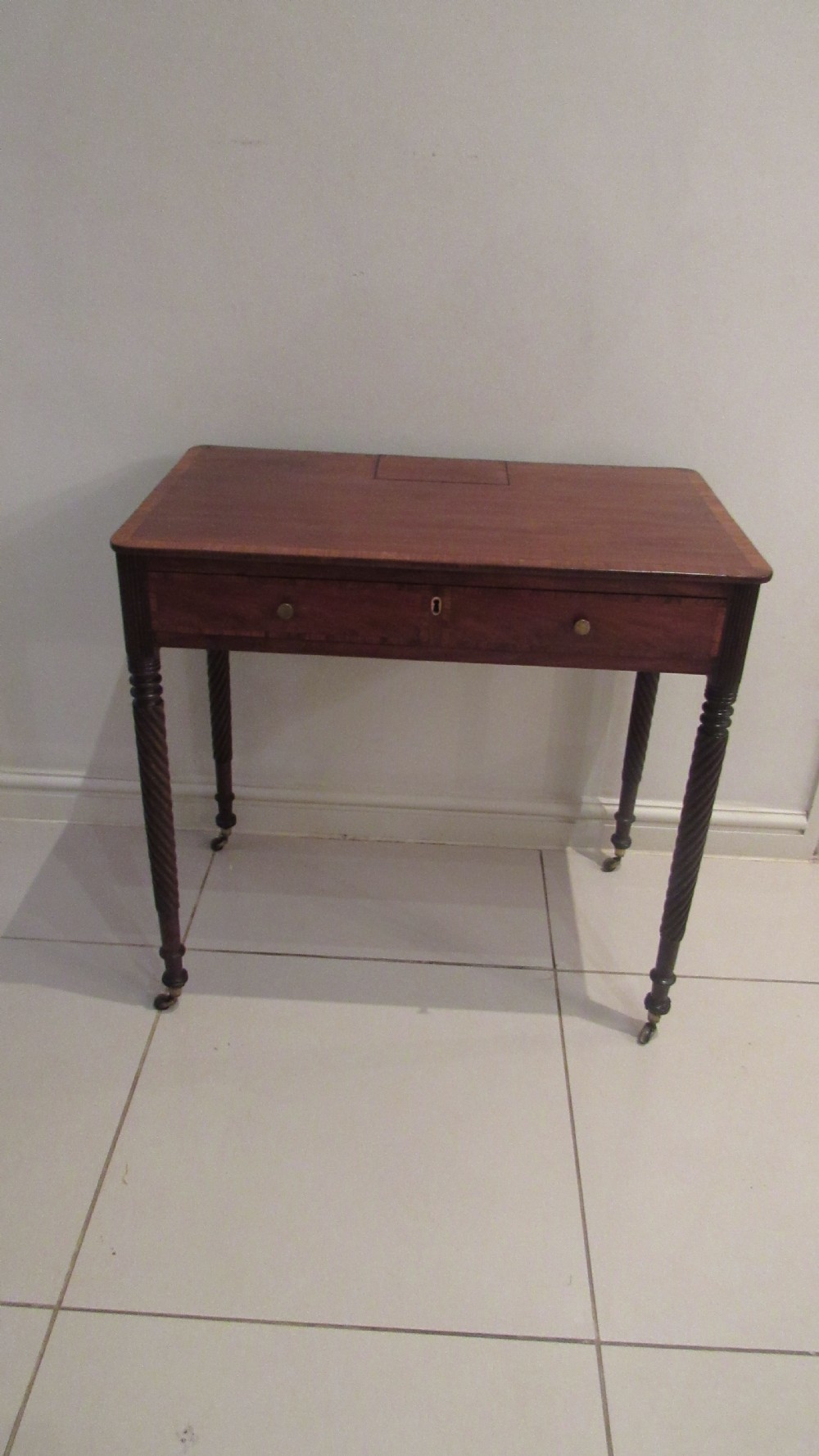 A Georgian mahogany chamber table featuring a rectangular top with a central flap, a single frieze drawer with brass hardware, and spiral turned legs on brass castors. View V