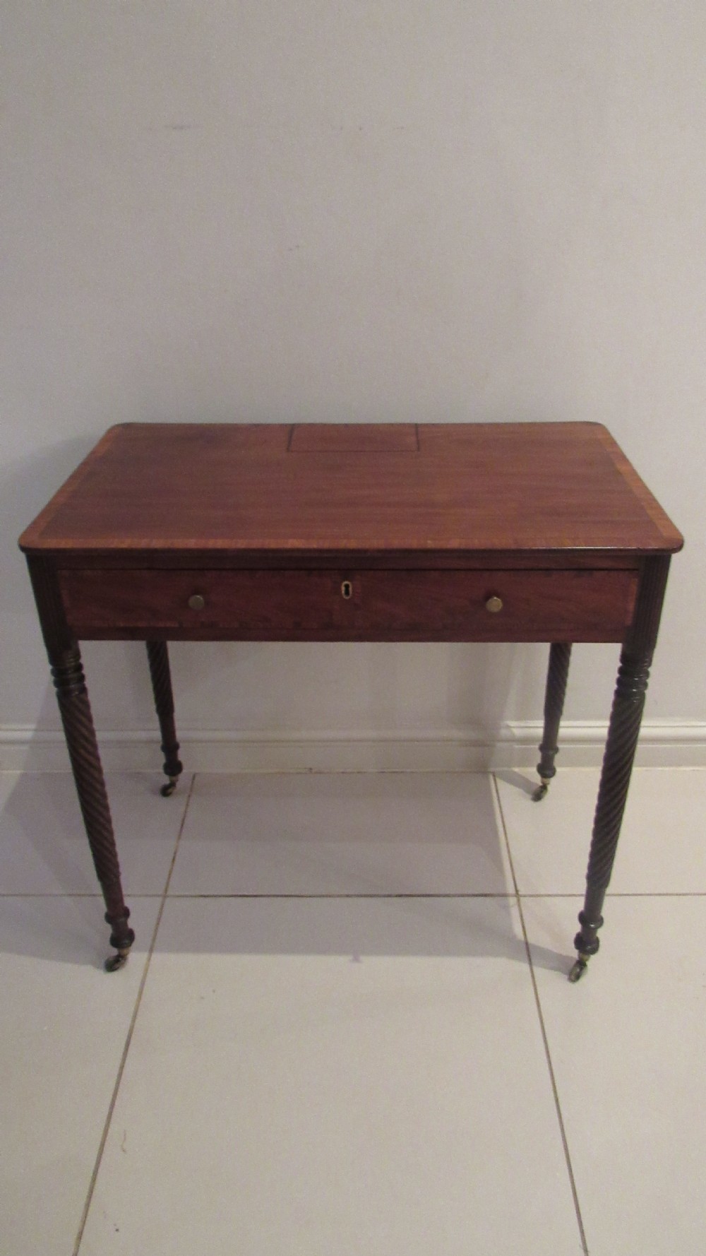 A Georgian mahogany chamber table featuring a rectangular top with a central flap, a single frieze drawer with brass hardware, and spiral turned legs on brass castors. View XIX