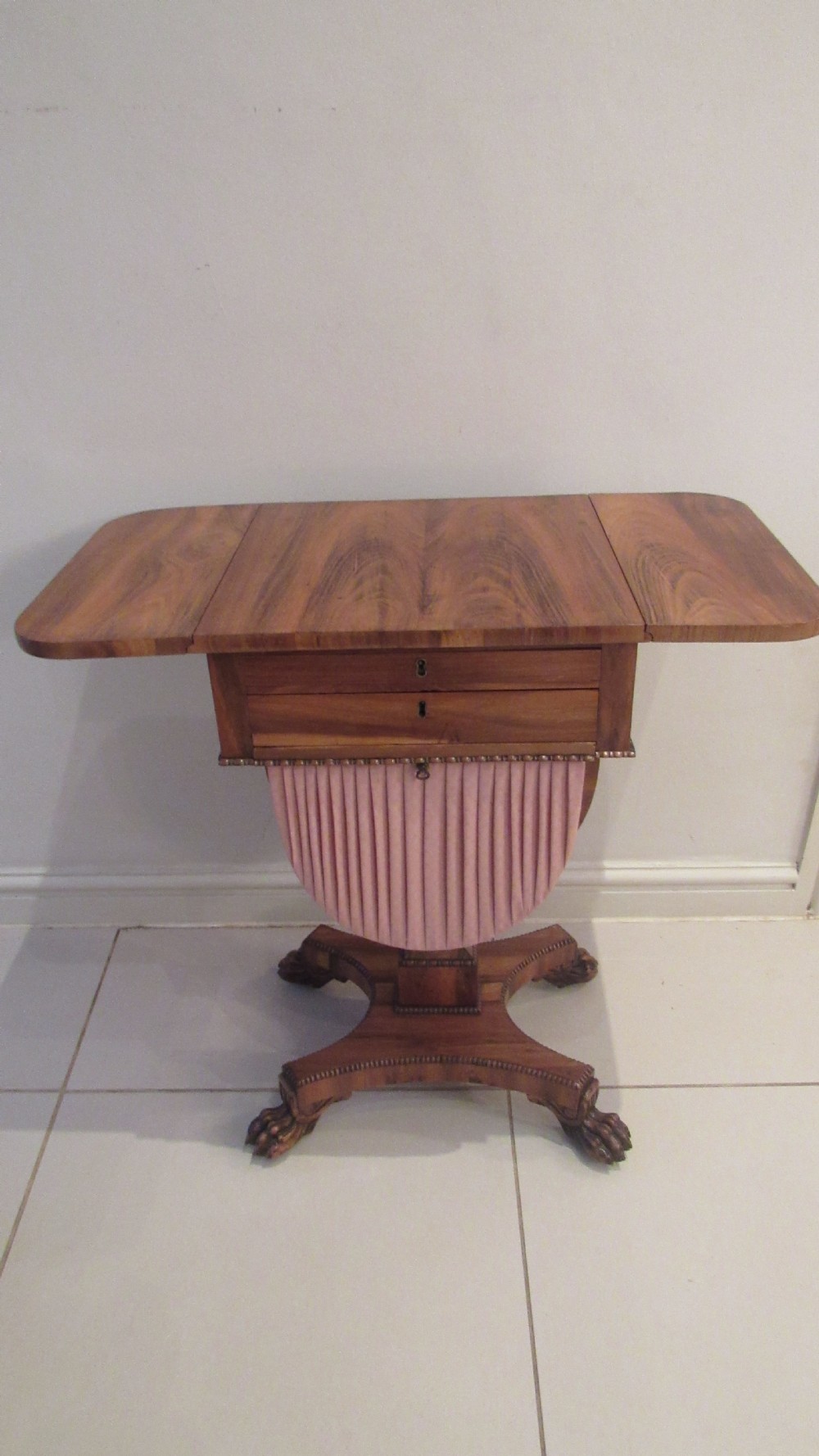 A William IV flame mahogany work table featuring drop-leaf side flaps, drawers with keyholes, a pleated pink fabric work well, and a quadruped base with carved paw feet. View II
