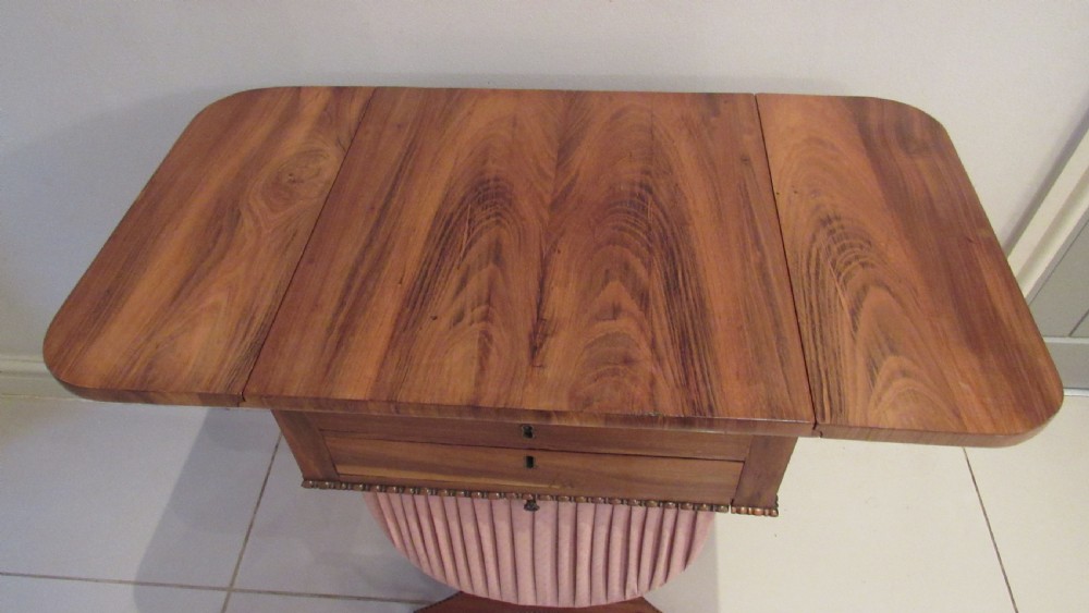 A William IV flame mahogany work table featuring drop-leaf side flaps, drawers with keyholes, a pleated pink fabric work well, and a quadruped base with carved paw feet. View VI