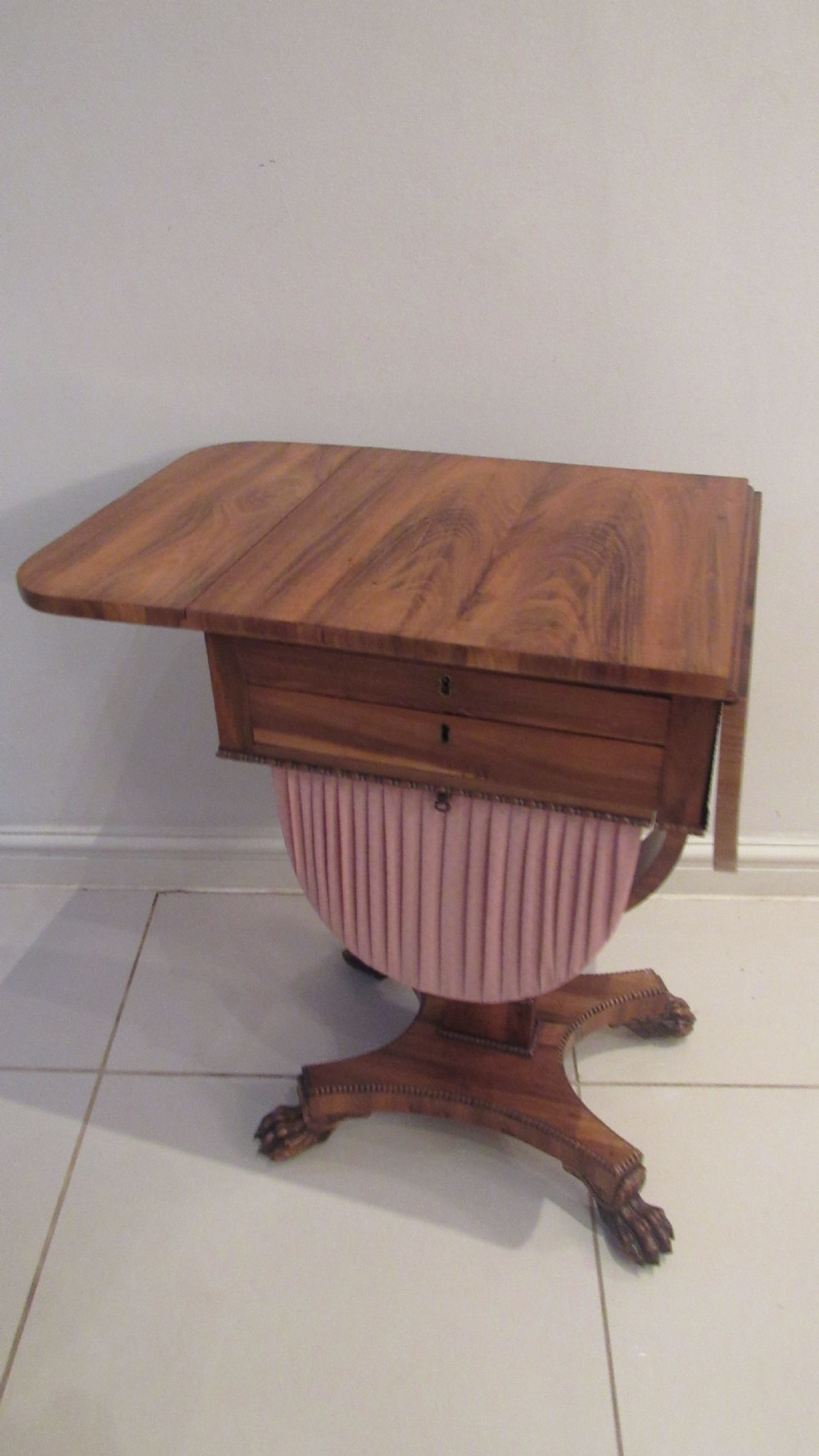 A William IV flame mahogany work table featuring drop-leaf side flaps, drawers with keyholes, a pleated pink fabric work well, and a quadruped base with carved paw feet. View XVIII