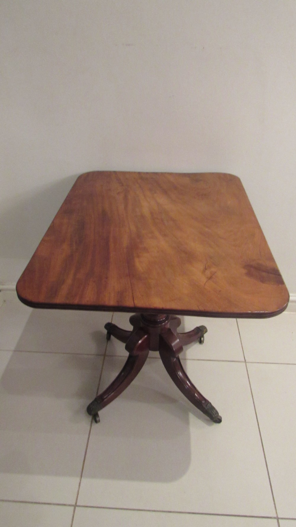 A Regency mahogany side table featuring a rectangular top with rounded corners, a central turned stem, and splayed legs with brass castors.