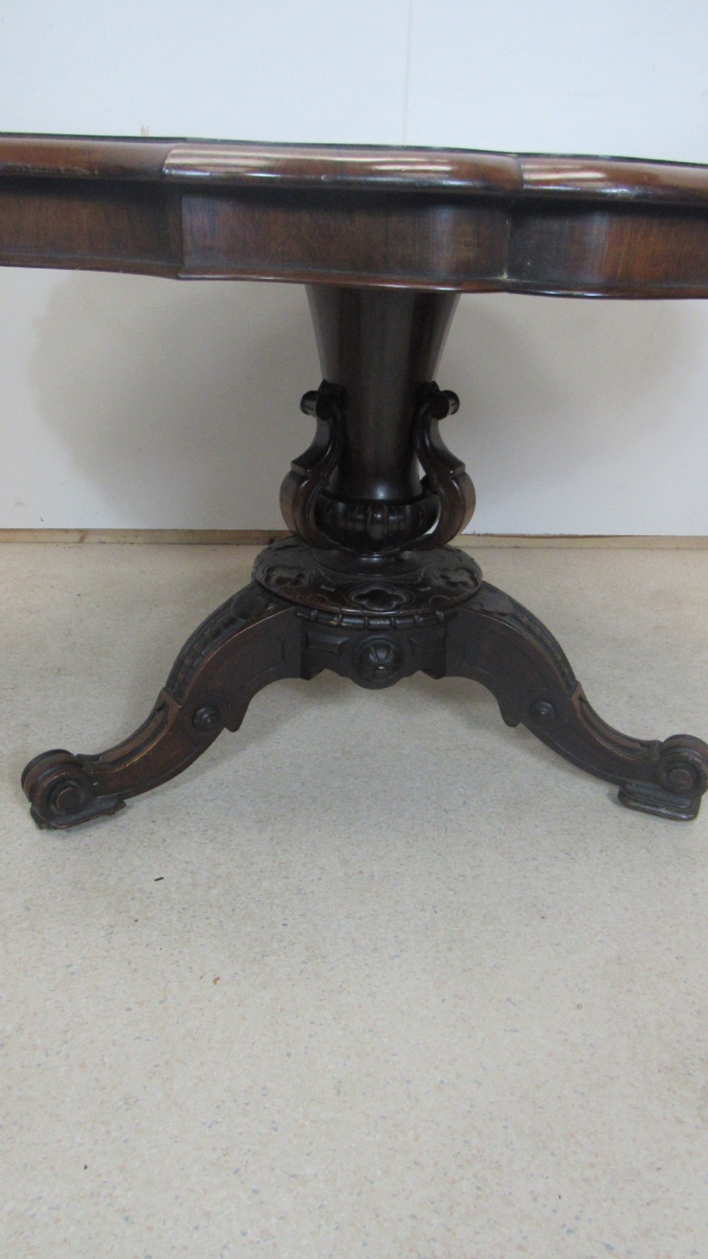 A 19th-century circular rosewood tilt-top table displayed in an upright position, featuring a shaped scalloped rim, prominent book-matched timber grain, and a carved pedestal base. View VII
