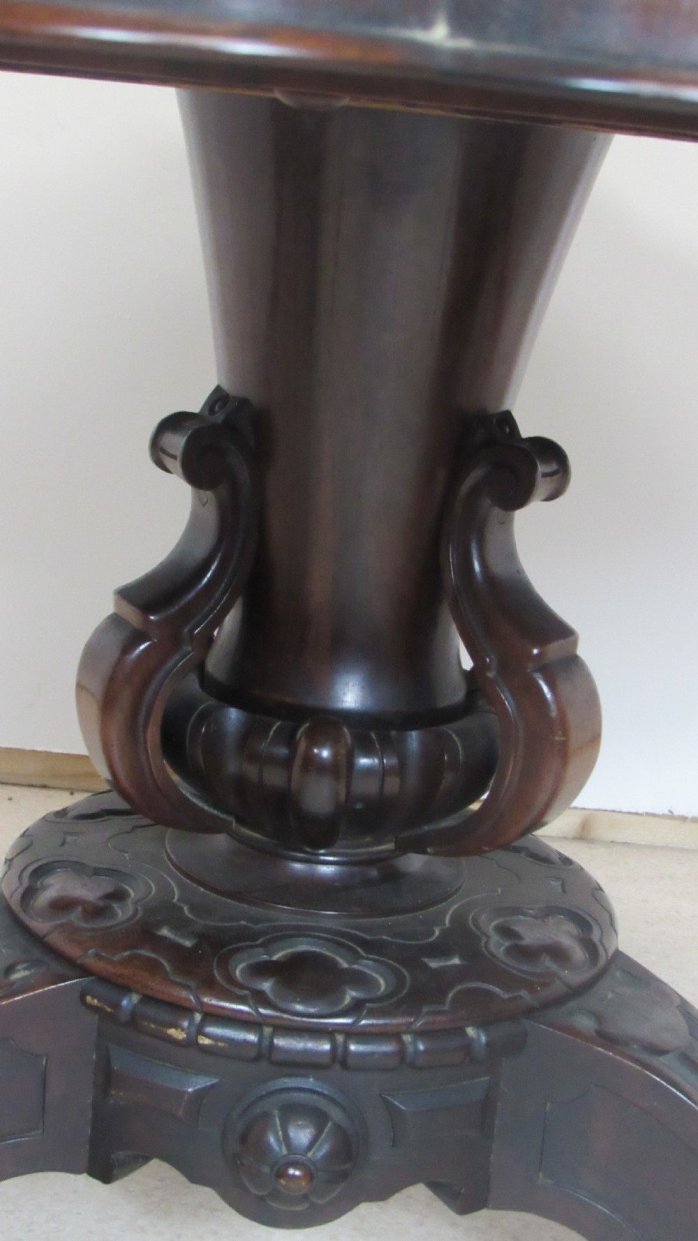 A 19th-century circular rosewood tilt-top table displayed in an upright position, featuring a shaped scalloped rim, prominent book-matched timber grain, and a carved pedestal base. View X