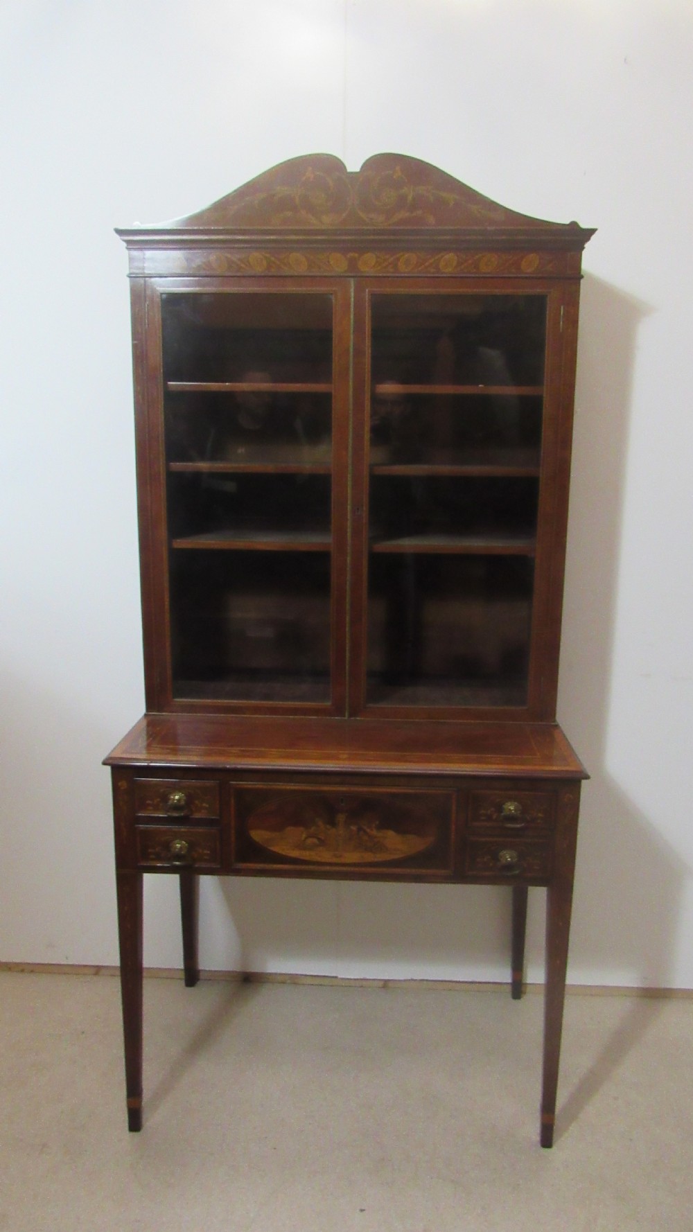An antique mahogany glazed display cabinet featuring marquetry inlay, two glass doors, four small drawers, and square tapered legs. View II